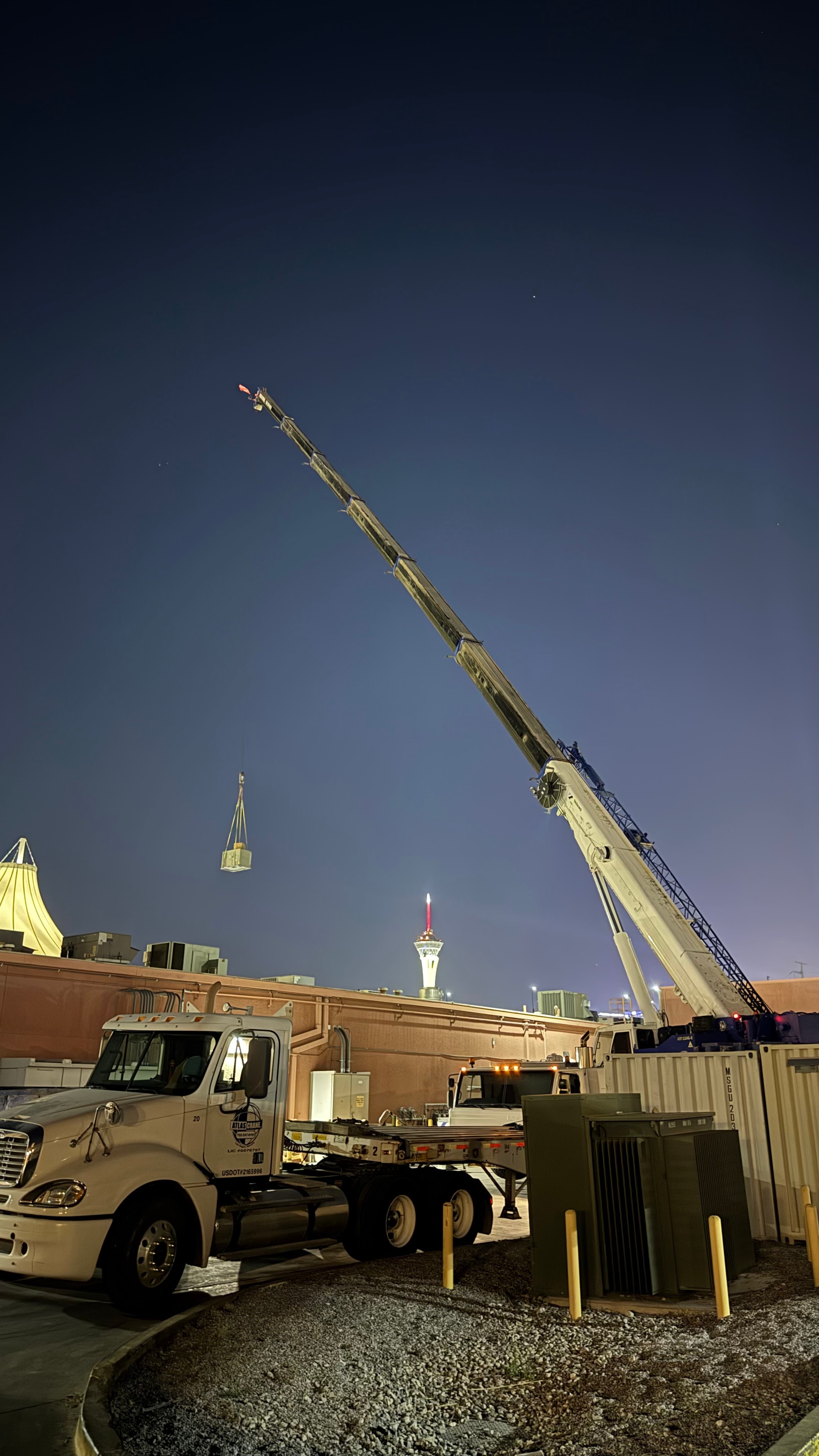 Nighttime crane set — rooftop unit lift with Strat Tower in background